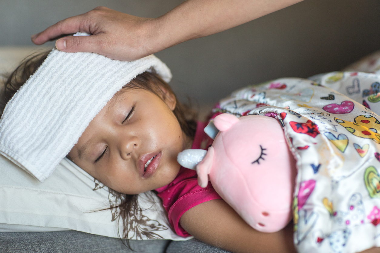 Young girl, sick in bed holding pink unicorn stuffed animal, with cloth over her head