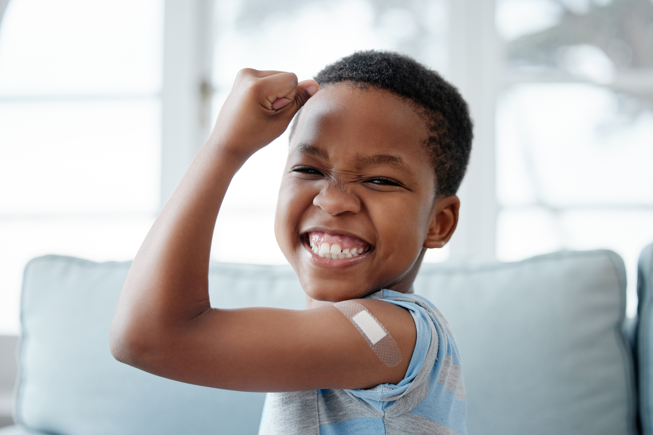 Young boy, flexing bicep with bandaid, proud after getting vaccine