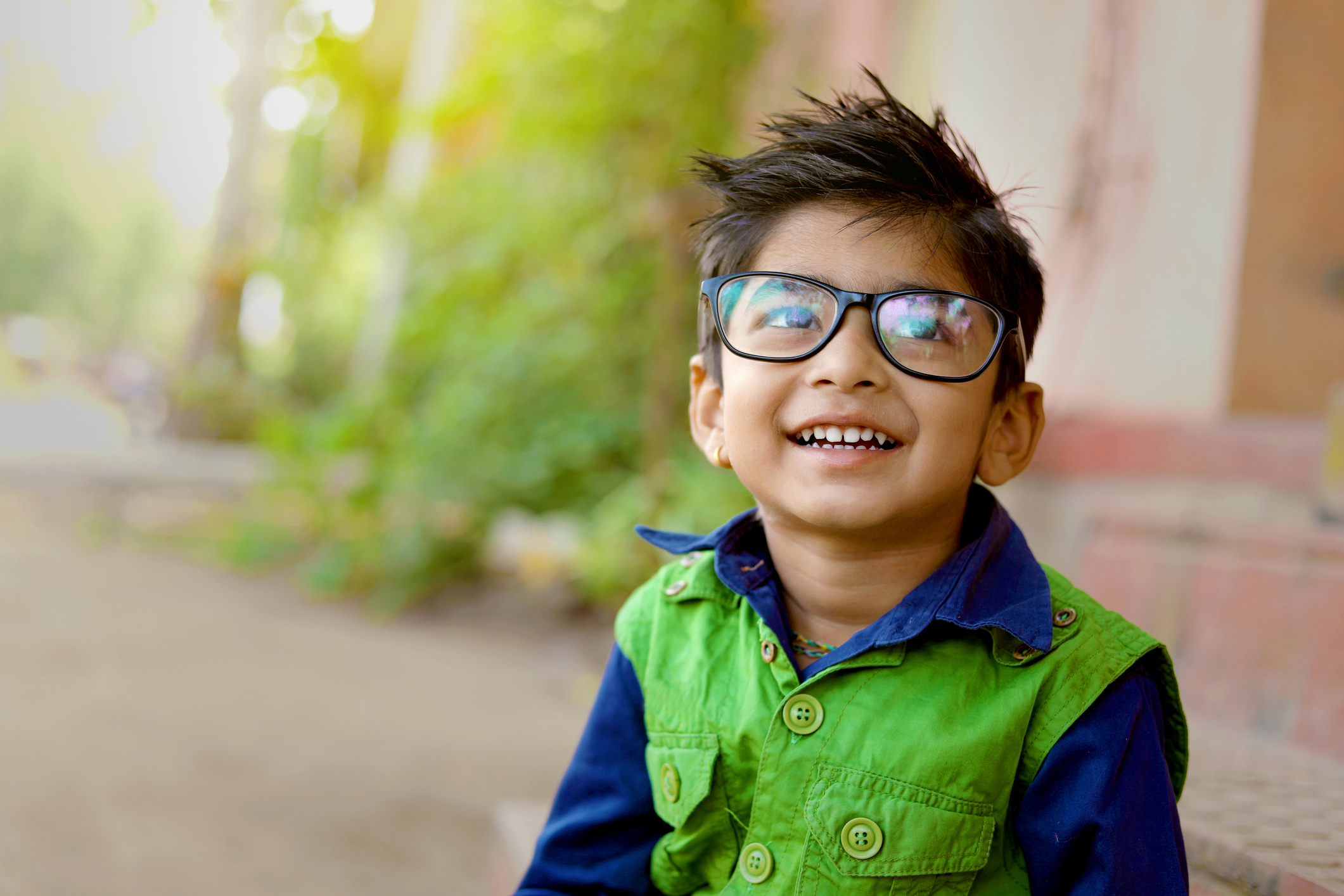 Young boy, smiling, looking up. Wearing glasses and green and blue jacket.
