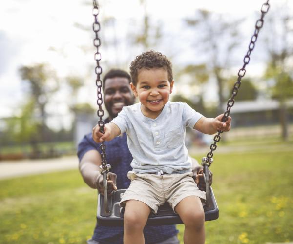 A dad and son playing on the swings together