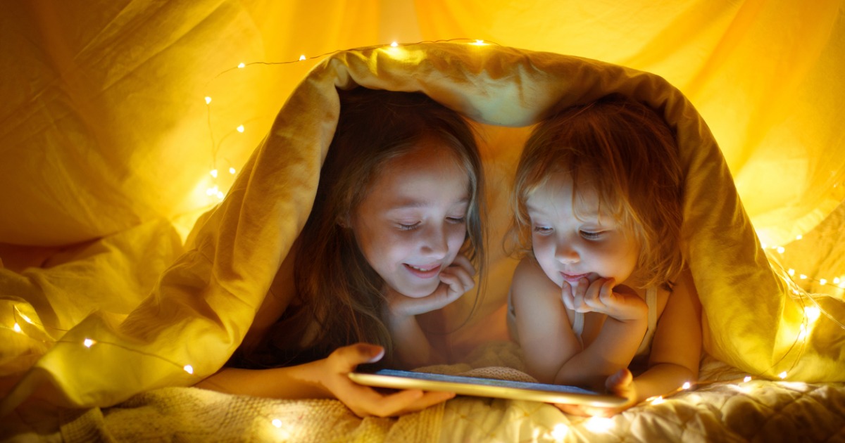 Two young girls hide under a blanket