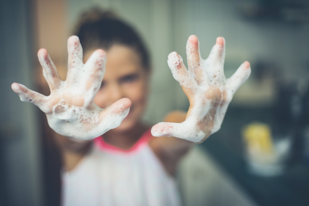 Girl holding up two soapy hands, handwashing facts