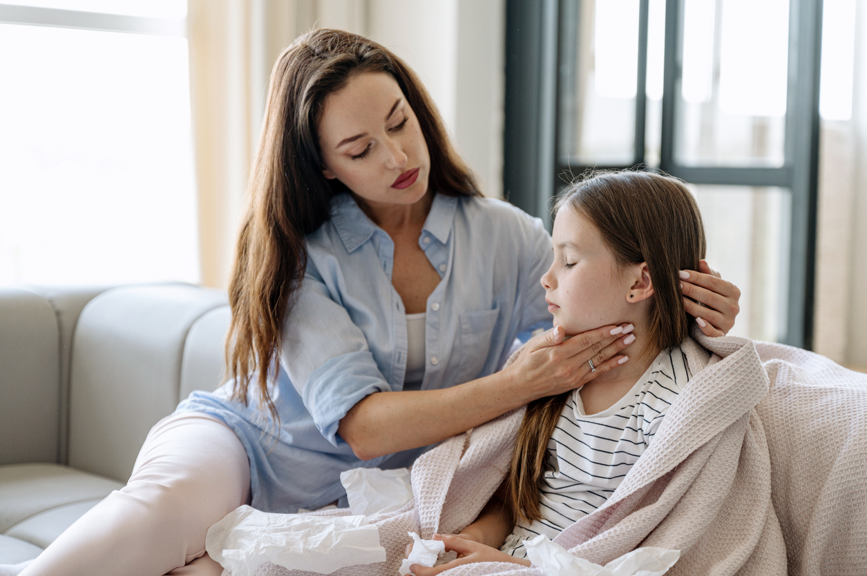 Mom on couch with young girl, massaging throat. Maybe strep throat.