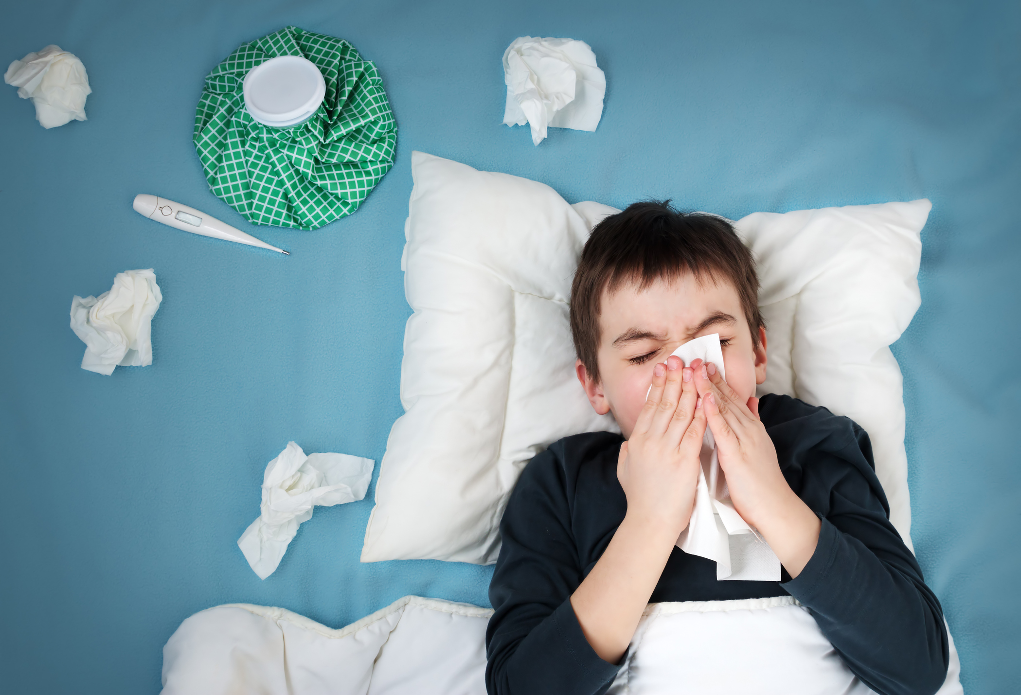 Young boy with bad cold in bed, blowing nose