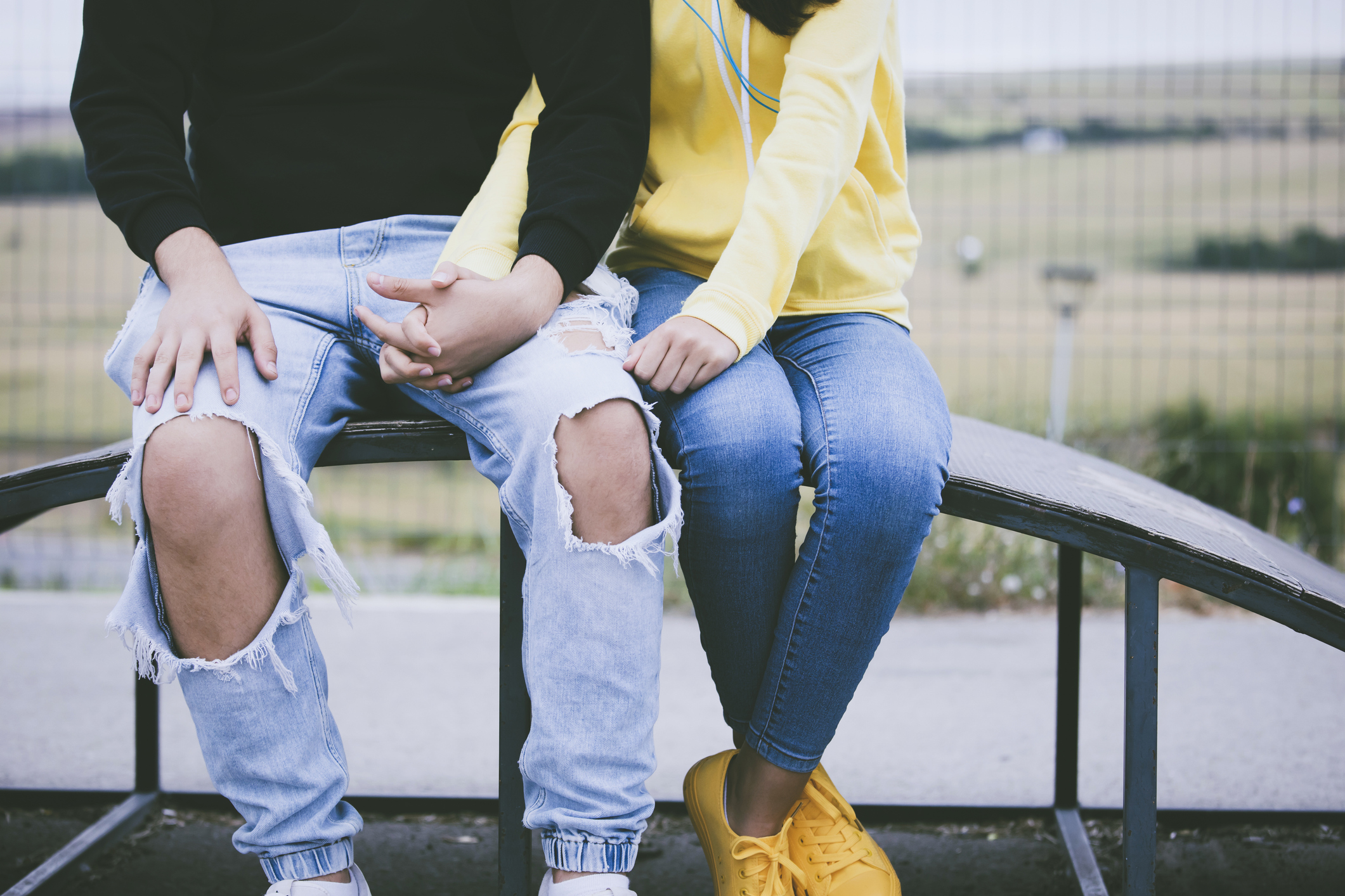 Two teens sitting and holding hands. 