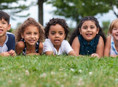 Kids laying down in the grass in a line