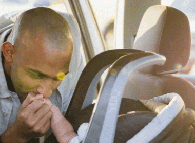 Dad kissing the hand of a child in a car seat