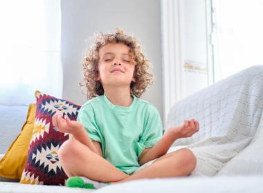 Young boy, practicing meditation on sofa, eyes shut, smiling