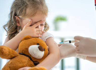 Young girl, scared, getting vaccine and holding teddy bear