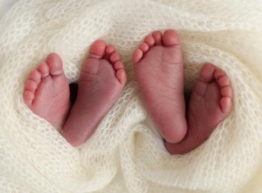 Two pairs of newborn twin feet sticking out from white blanket