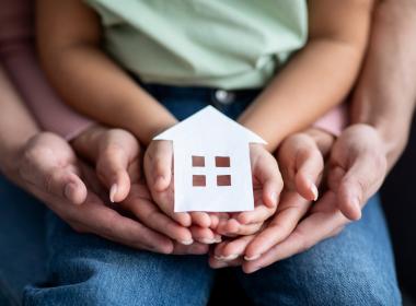 Hands holding a paper cutout of a house.