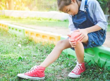 Young girl outside grabbing knee, joint pain and arthritis in kids