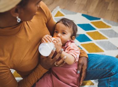 Baby drinking bottle in mother's arms.