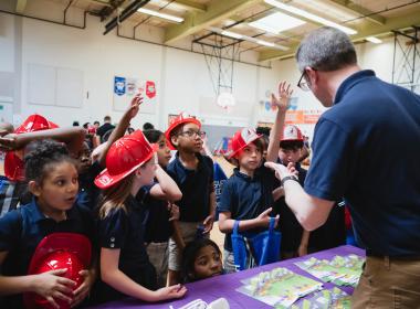 School-aged kids holding red safety hats at gun safety conference