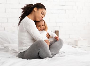 Mom holding whiny infant on bed, trying to soothe them