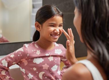 Mom applying lotion on young girl's face. Safe skincare for kids and teens
