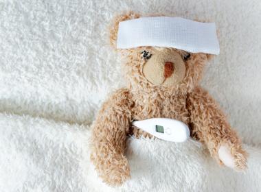 Stuffed teddy bear with cloth over its forehead and thermometer under arm, fever emergency