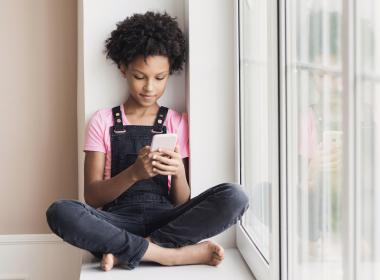 Preteen girl sitting down at window looking at smart phone