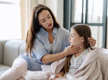 Mom on couch with young girl, massaging throat. Maybe strep throat.