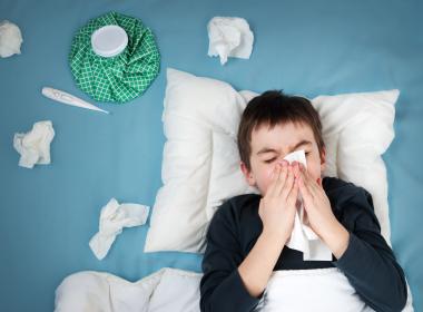 Young boy with bad cold in bed, blowing nose