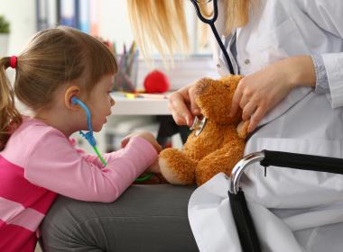 Young girl listening to teddy bear's heart on doctor's lap