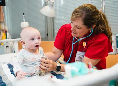 A baby inpatient in the cardiac ICU is examined by his doctor. A baby inpatient in the cardiac ICU is examined by his doctor.