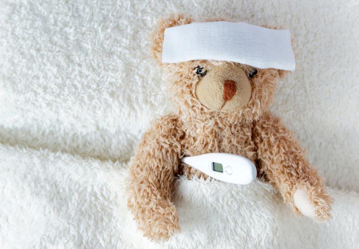 Stuffed teddy bear with cloth over its forehead and thermometer under arm, fever emergency