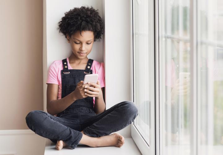 Preteen girl sitting down at window looking at smart phone