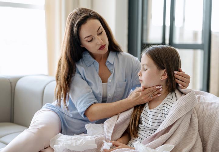 Mom on couch with young girl, massaging throat. Maybe strep throat.