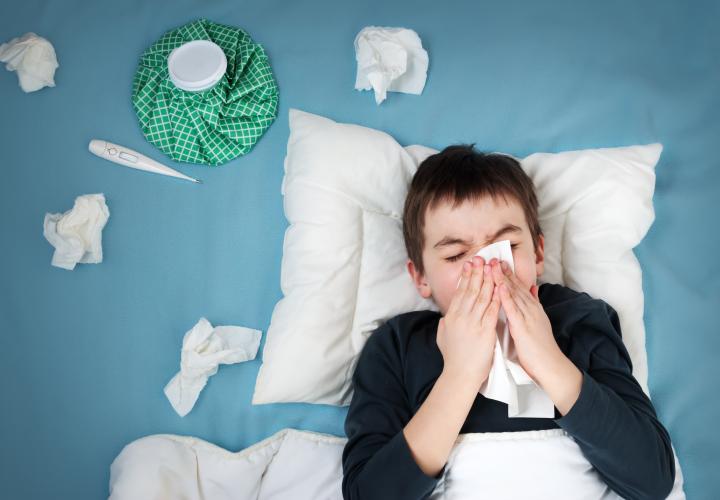 Young boy with bad cold in bed, blowing nose