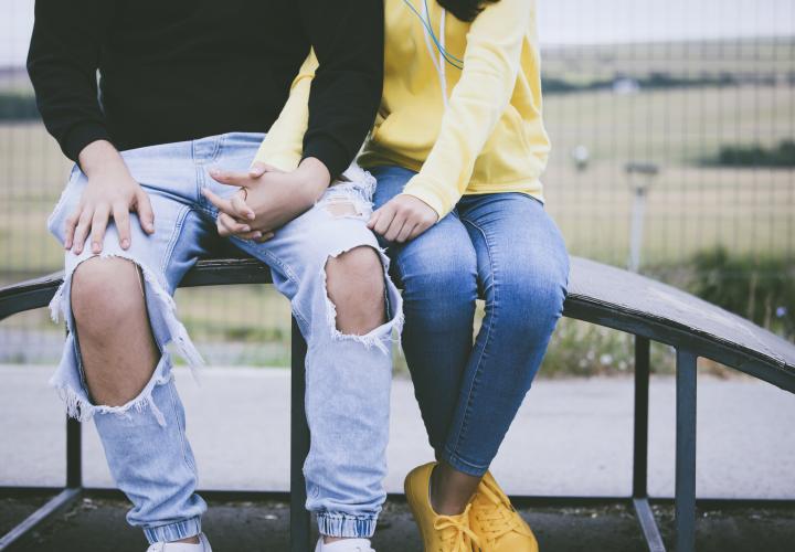 Two teens sitting and holding hands. 