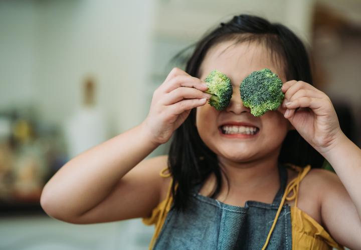 A child holding broccoli up to their face.