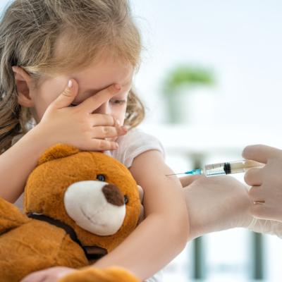 Young girl, scared, getting vaccine and holding teddy bear