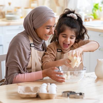 Mom and young daughter crack eggs into a bowl in kitchen, happily.