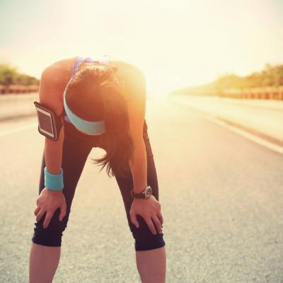 Young adult female runner bent over, overheated, outside