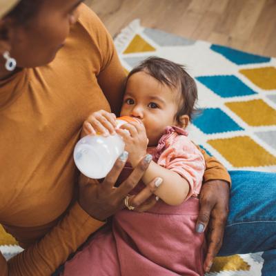 Baby drinking bottle in mother's arms.