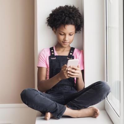 Preteen girl sitting down at window looking at smart phone