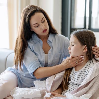 Mom on couch with young girl, massaging throat. Maybe strep throat.