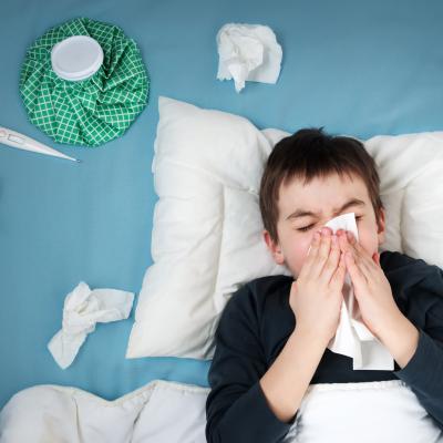 Young boy with bad cold in bed, blowing nose