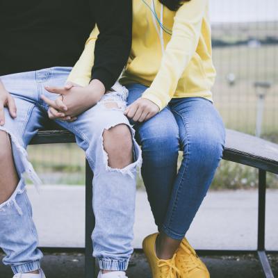 Two teens sitting and holding hands. 