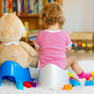 Cute toddler girl sitting on potty next to stuffy on its potty. Backs only