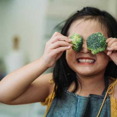 A child holding broccoli up to their face.