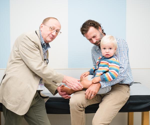 A neurology patient is examined by his doctor while his dad holds him.