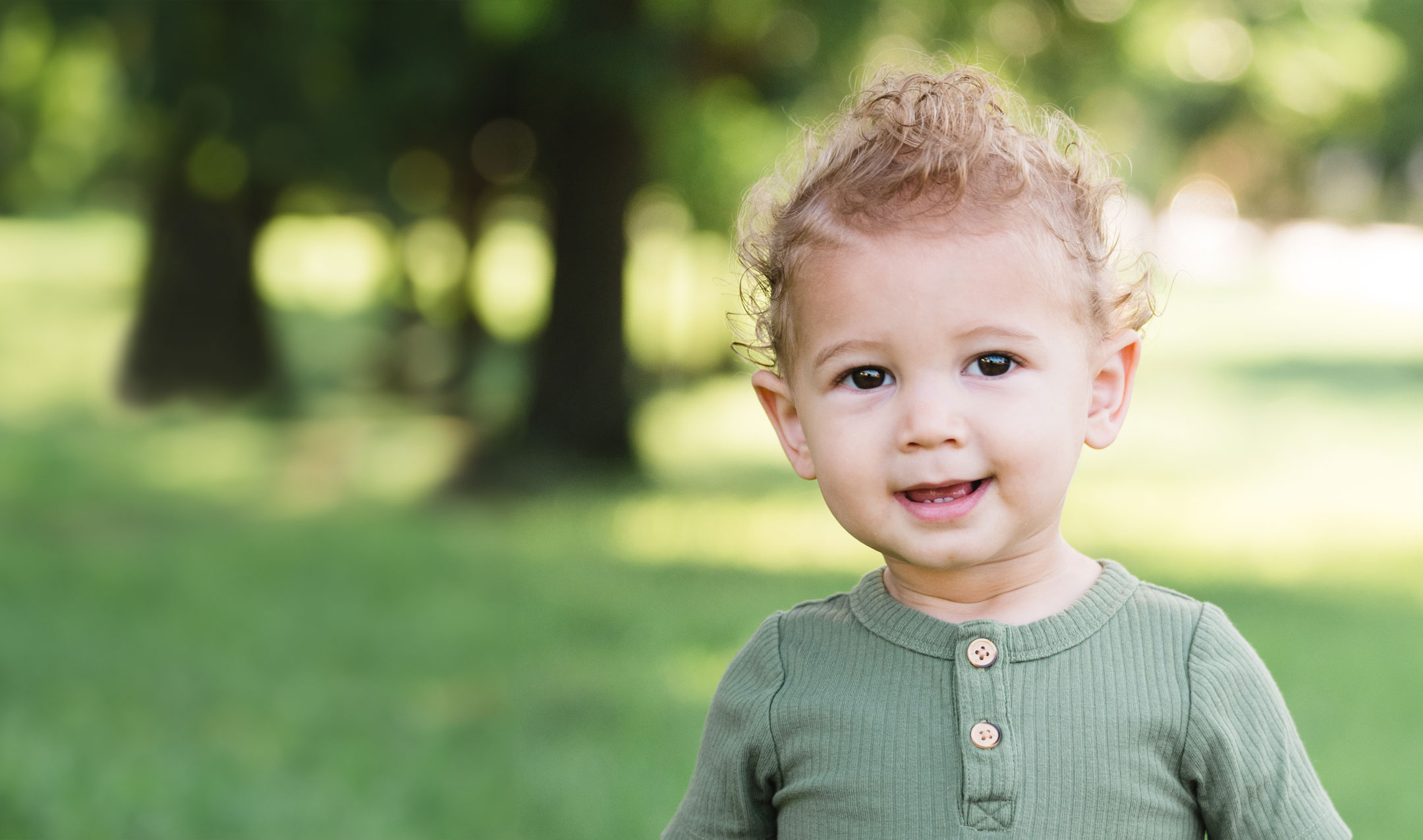 young child smiling in an outside grassy area
